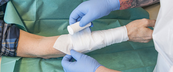 Anlegen eines Verbands am Unterarm des Patienten