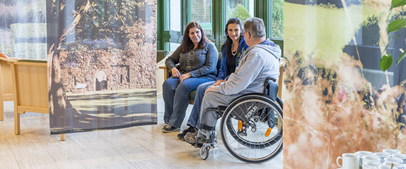 Patient im Rollstuhl mit zwei Besucherinnen