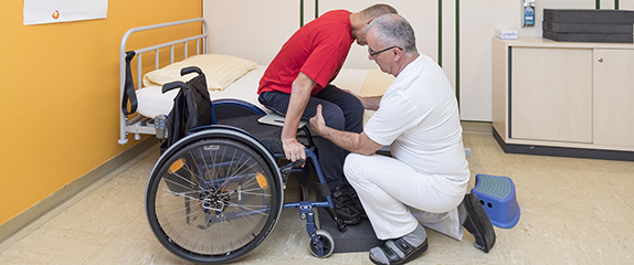 Patient wird unterstützt beim Umsetzen vom Rollstuhl aufs Betttuhl.