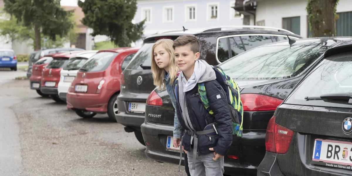 Zwei Kinder befinden sich vor einigen geparkten Autos und möchten die Straße überqueren. Zwei Kinder befinden sich vor einigen geparkten Autos und möchten die Straße überqueren.