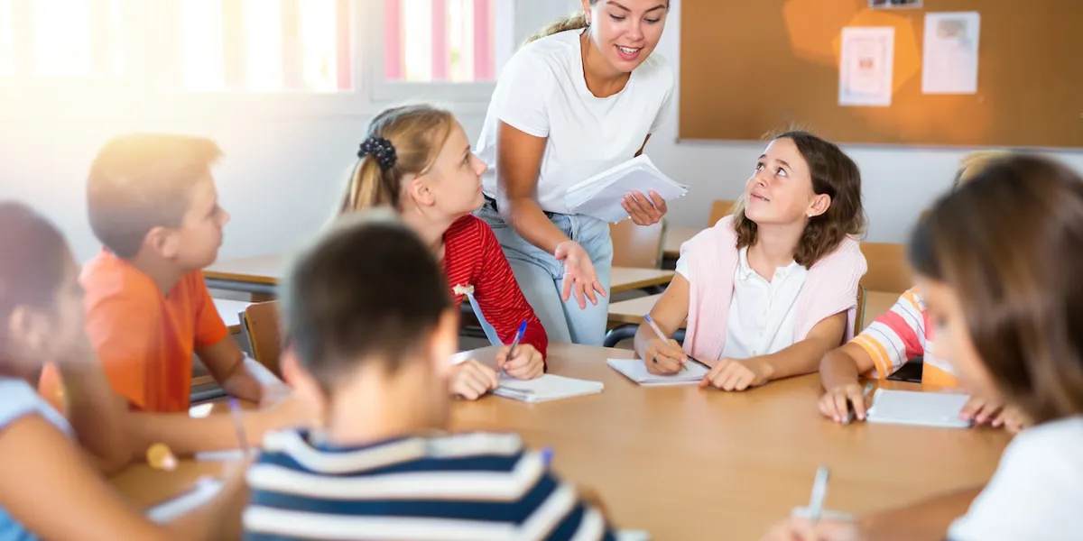 Gruppe Schüler:innen an einem runden Tisch Eine Gruppe Schüler:innen an einem runden Tisch erhält von der Lehrperson gerade eine Erklärung
