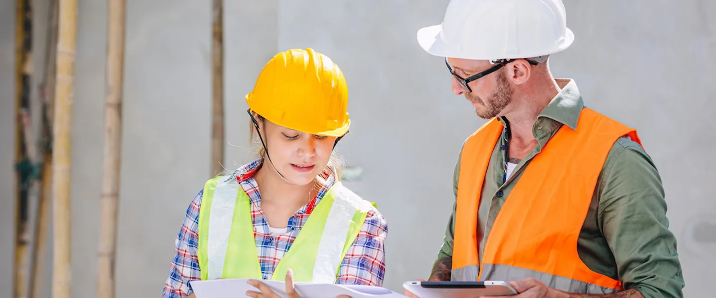 Zwei Bauarbeiter:innen besprechen sich auf einer Baustelle