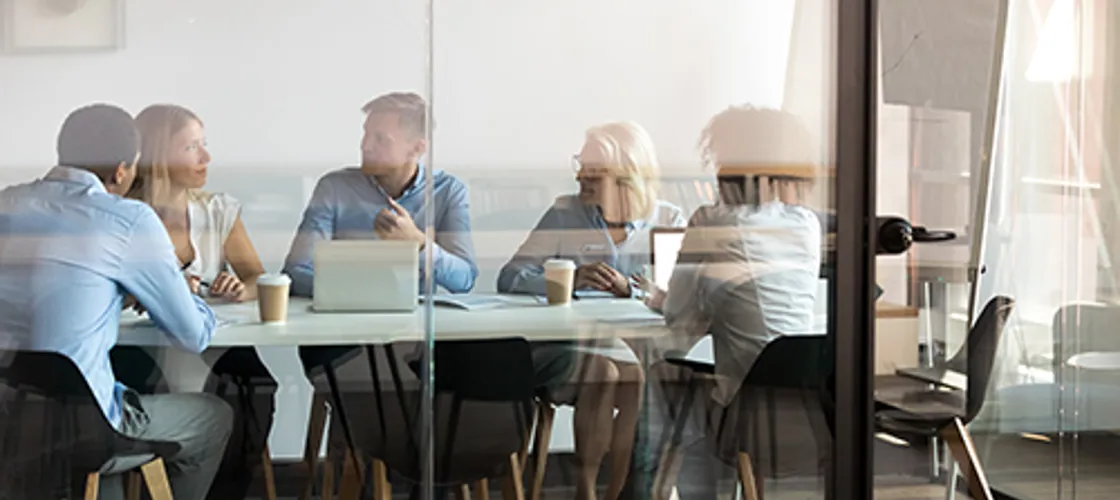 Fünf Personen befinden sich in einem Büro-Besprechungsraum in einem Meeting
